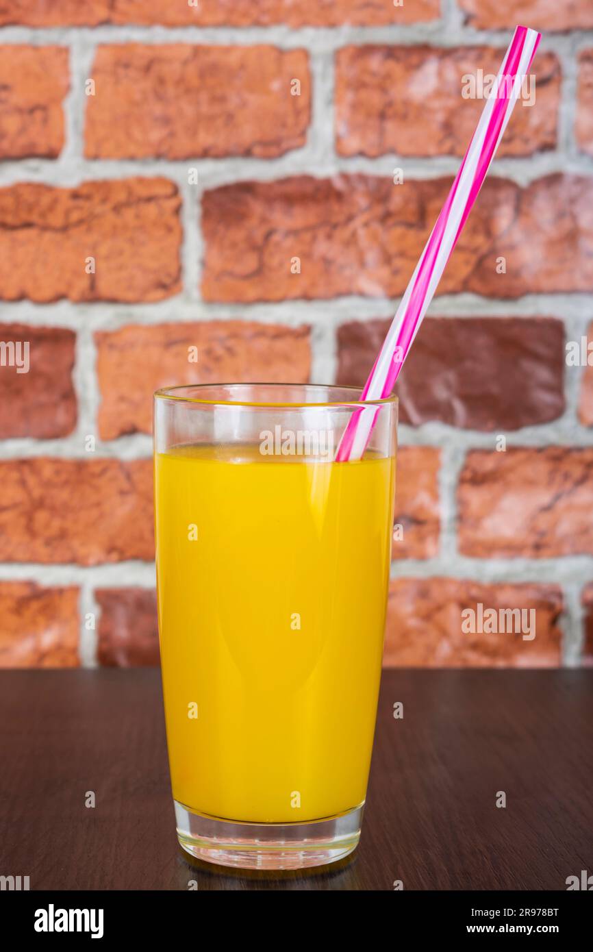 Succo d'arancia in una tazza di vetro con un tubo su un tavolo di legno e uno sfondo di una parete di mattoni arancioni Foto Stock