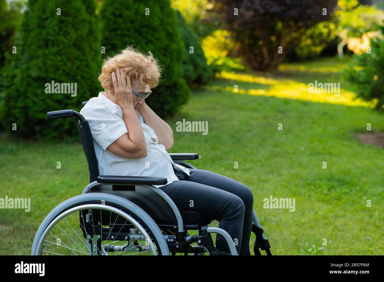 Donna anziana infelice che piange mentre si siede su una sedia a rotelle in una passeggiata all'aperto. Foto Stock