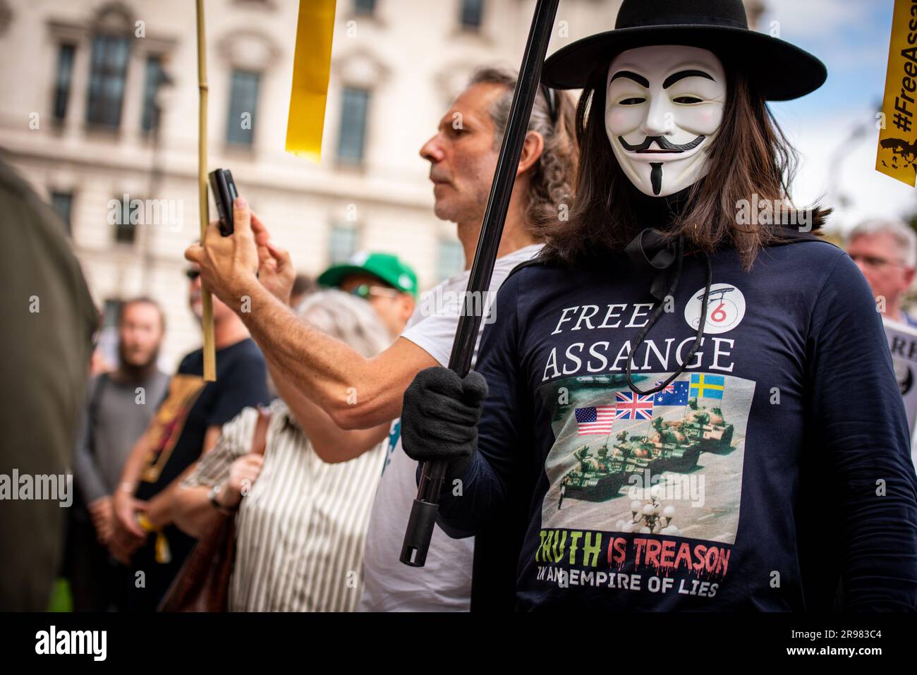 Un protestore mascherato partecipa al “qualcosa da dire?” Protesta gratuita di Julian Assange a Parliament Square a Londra. "Qualcosa da dire?" È una scultura in bronzo a grandezza naturale che ritrae tre figure, ognuna in piedi su una sedia dell'artista Davide Dormino. La quarta sedia è vuota perché è la nostra sedia. Quella che ci ha permesso di esprimere noi stessi o semplicemente di stare accanto a Edward Snowden, Julian Assange e Chelsea Manning, che hanno avuto il coraggio di dire di no all'intrusione della sorveglianza globale e alle bugie che portano alla guerra. Foto Stock