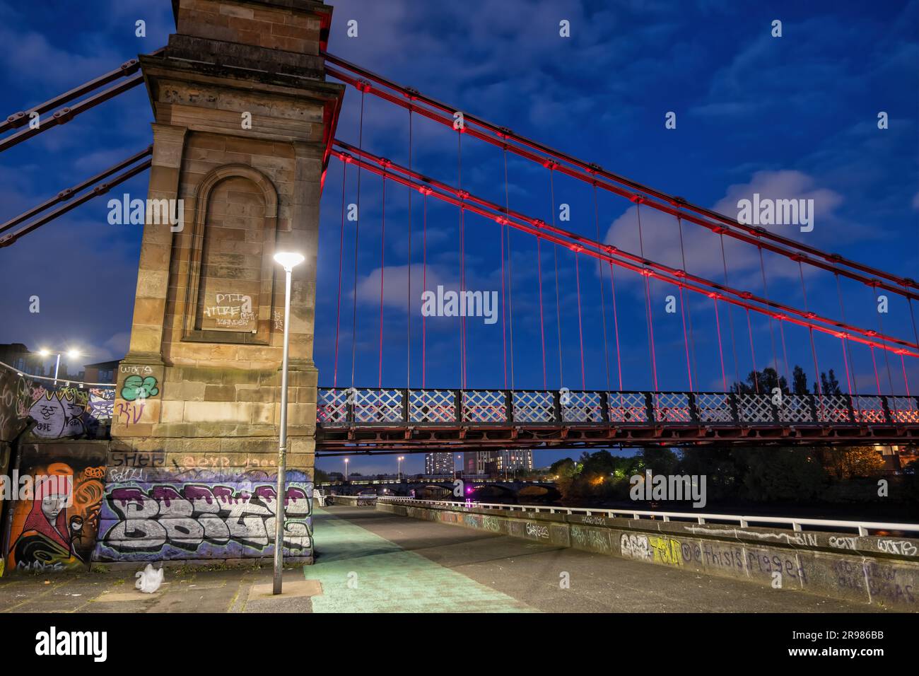 Il South Portland Street Suspension Bridge di notte, passerella sul fiume Clyde nella città di Glasgow, Scozia, Regno Unito. Torre di pietra arenaria e i battuto Foto Stock