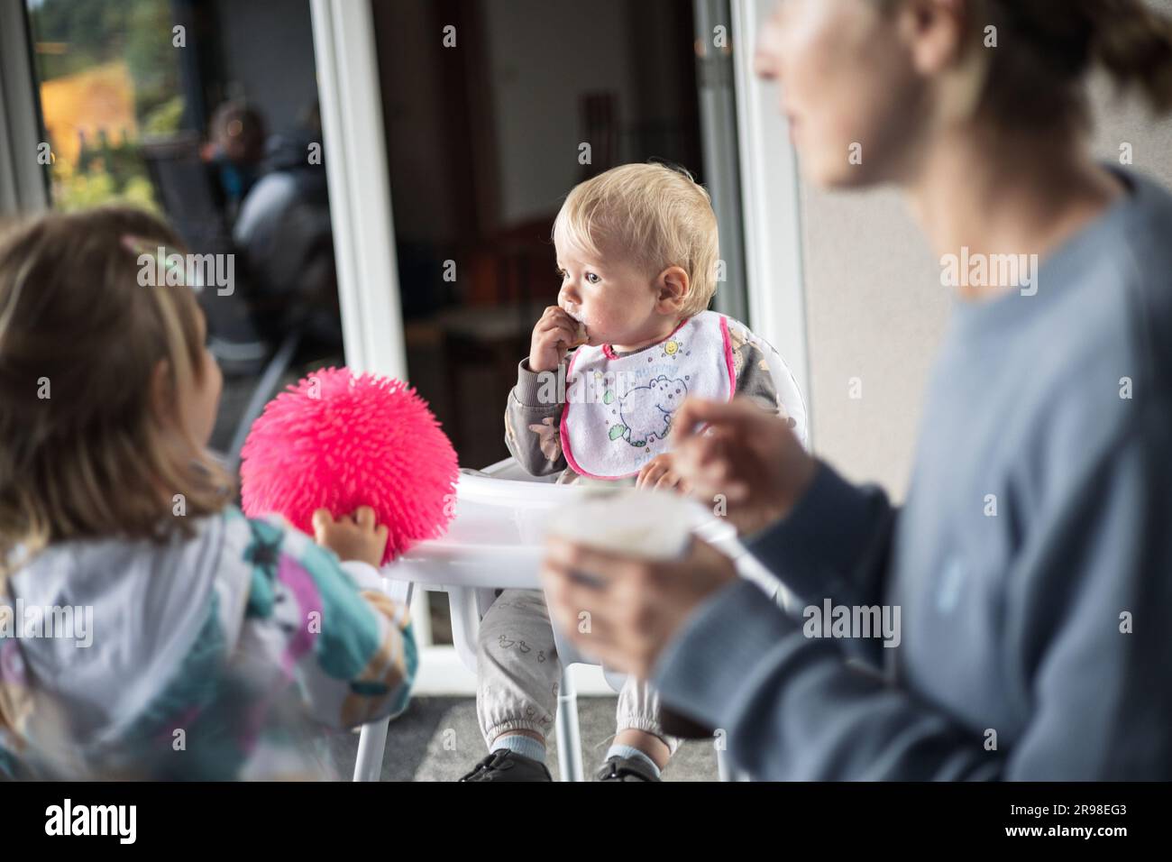 Cucchiaio per la madre che dà da mangiare al bambino in seggiolone con purea di frutta al tavolo da pranzo a casa. Concetto introduttivo di alimenti solidi per bambini. Foto Stock