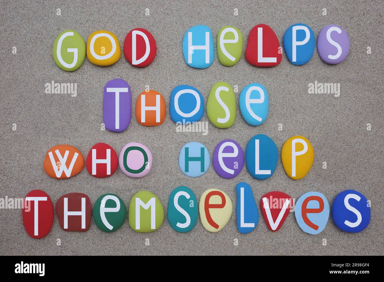Dio aiuta coloro che si aiutano da soli, citazione motivazionale composta da lettere di pietra dipinte a mano su sabbia verde Foto Stock