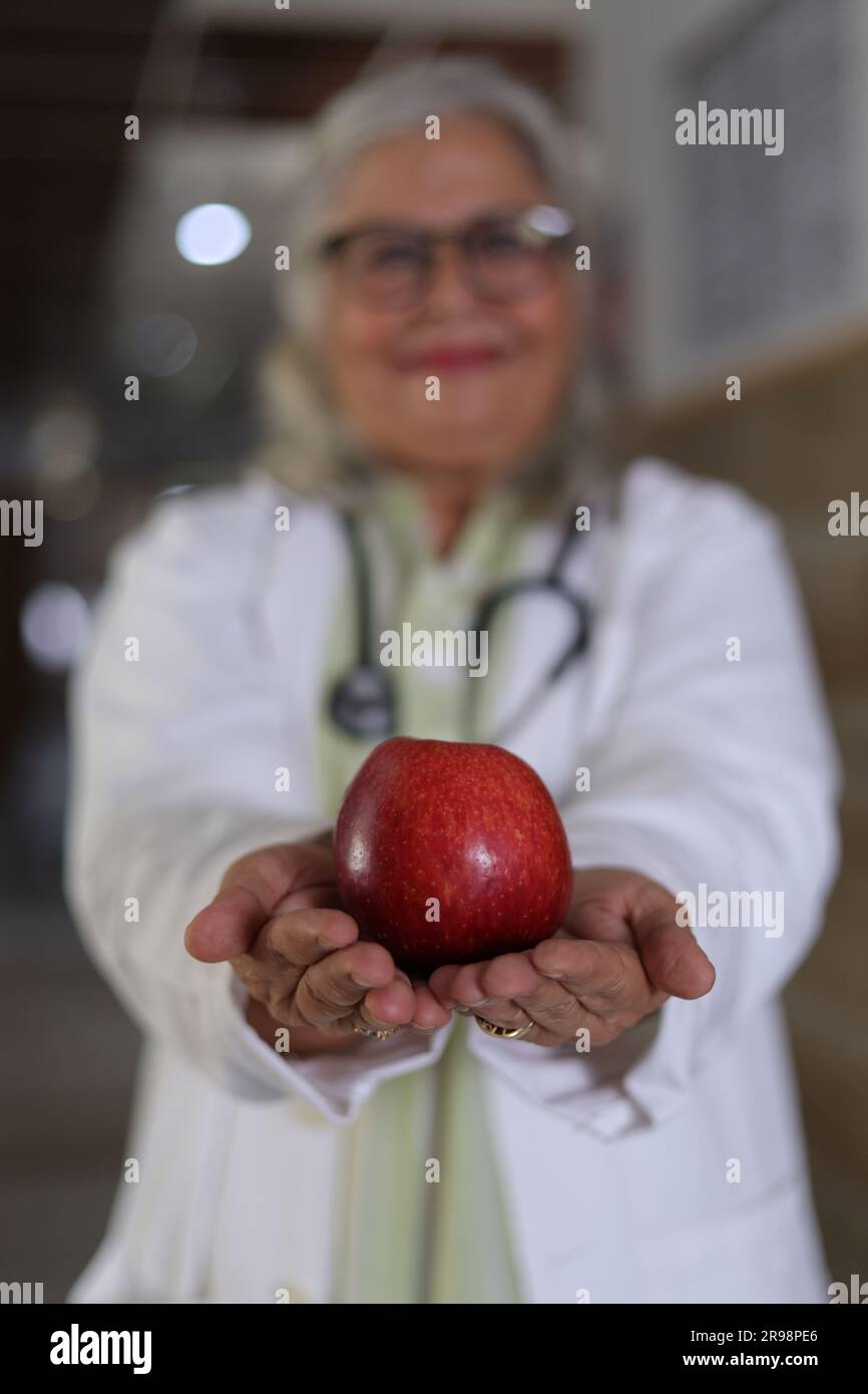 ritraendo il messaggio di avere una salute migliore e un programma dietetico molto sano. Attraente medico femminile con un cappotto bianco sorridente e con in mano una mela. Foto Stock