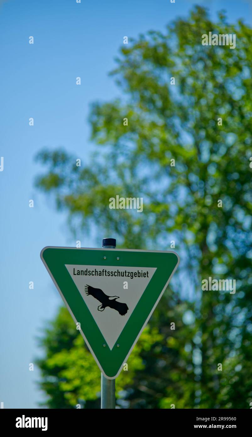 Cartello triangolare verde-bianco con la scritta "Landschaftsschutzgebiet" (tedesco per l'area di conservazione del paesaggio) di fronte a un albero verde e a un cielo azzurro Foto Stock