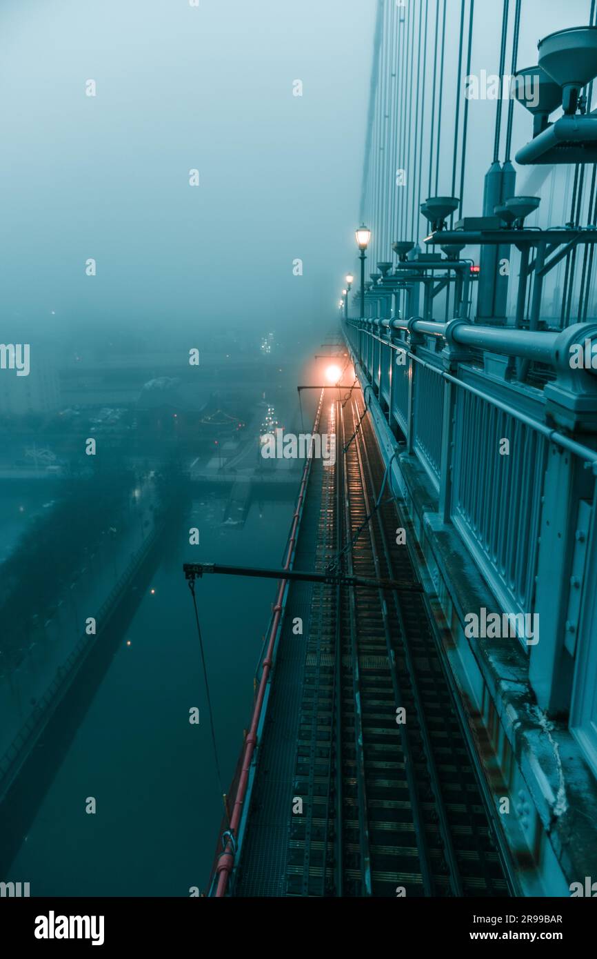 Un treno passa sotto un ponte avvolto dalla nebbia, creando un'atmosfera misteriosa e inquietante Foto Stock