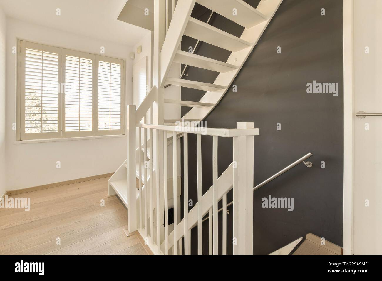 una scala con ringhiere bianche e pavimento in legno in uno stile moderno, l'ingresso alle scale e' dipinto di nero Foto Stock