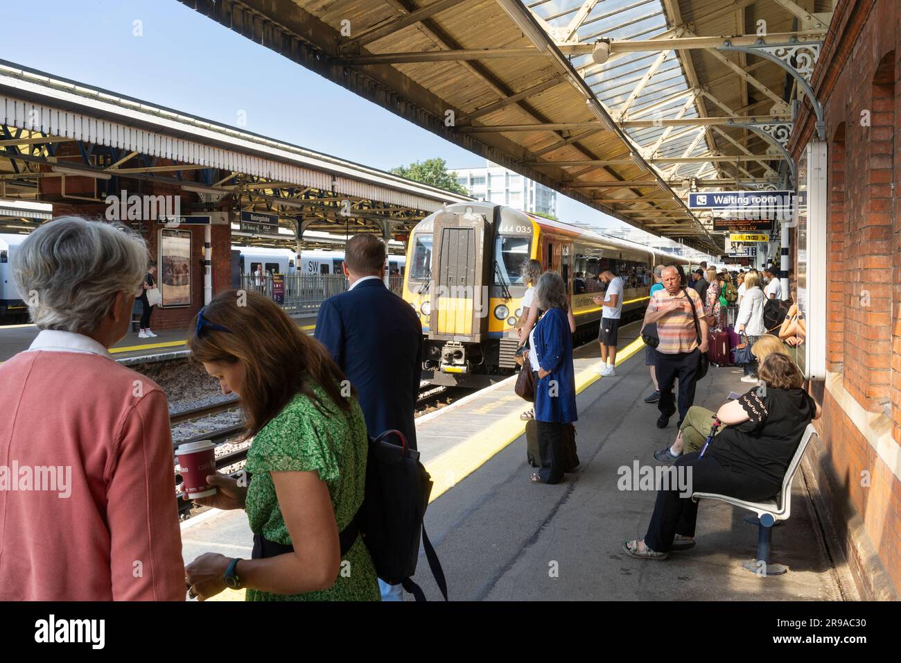 Il venerdì pendolari e viaggiatori in treno aspettano su un binario alla stazione ferroviaria di Basingstoke per l'arrivo di un treno della South Western Railway. Inghilterra Foto Stock