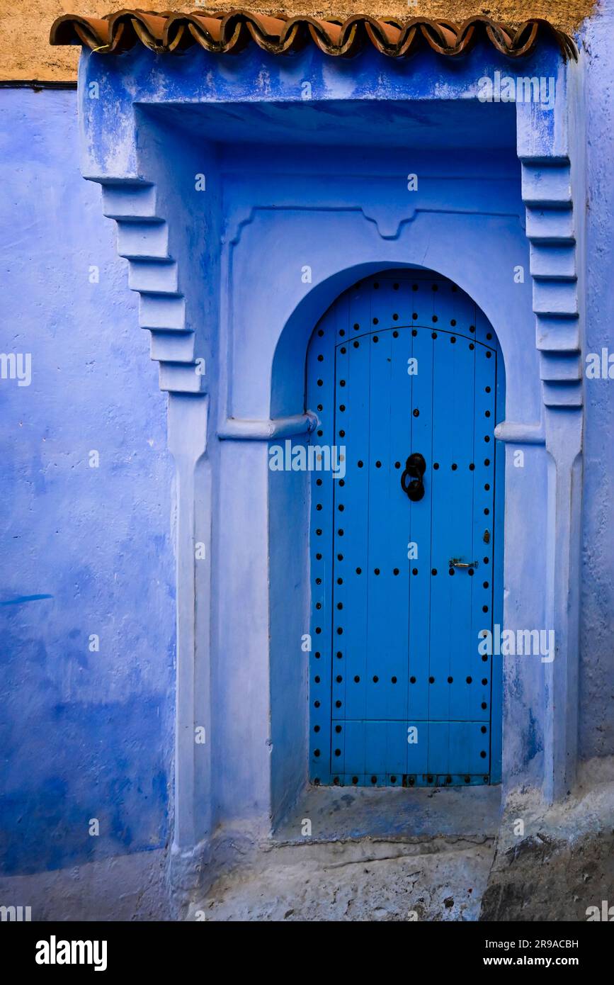 Un muro esterno e una formidabile porta d'ingresso in legno ad arco sono sfumature di blu, che ben rappresentano la città Blu, l'antica Chefchaouen, Marocco Foto Stock