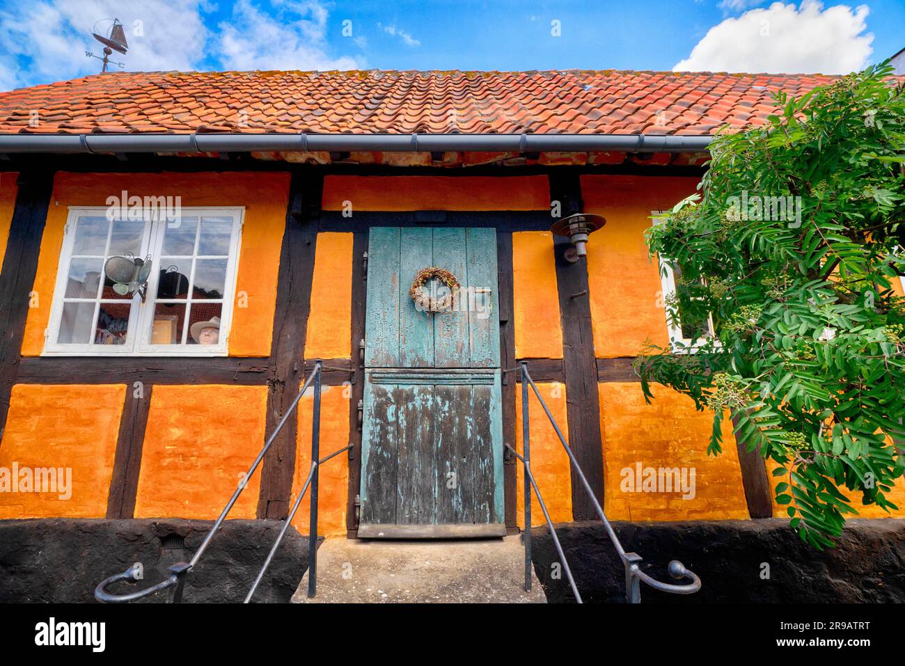 Ingresso di una vecchia casa arancione sotto un cielo blu in estate con un albero verde nella parte anteriore Foto Stock