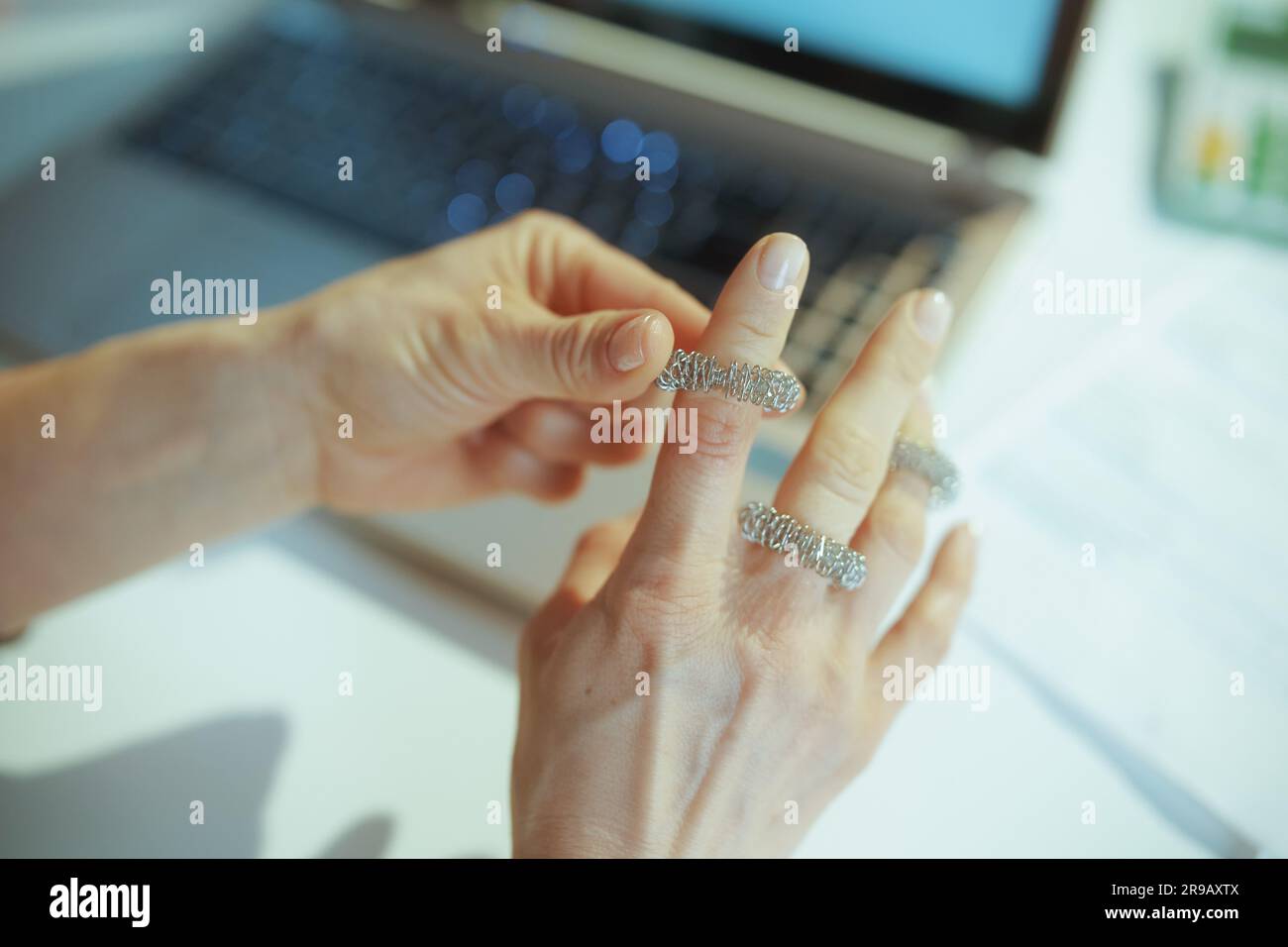 Ambiente di lavoro sostenibile. Primo piano su una moderna donna proprietaria di una piccola impresa in un abito da lavoro grigio nel moderno ufficio verde con massaggiatore per le dita. Foto Stock