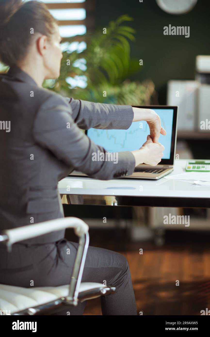 Ambiente di lavoro sostenibile. Visto da dietro moderna donna di affari in un vestito grigio di affari in moderno verde ufficio che stretching mano. Foto Stock