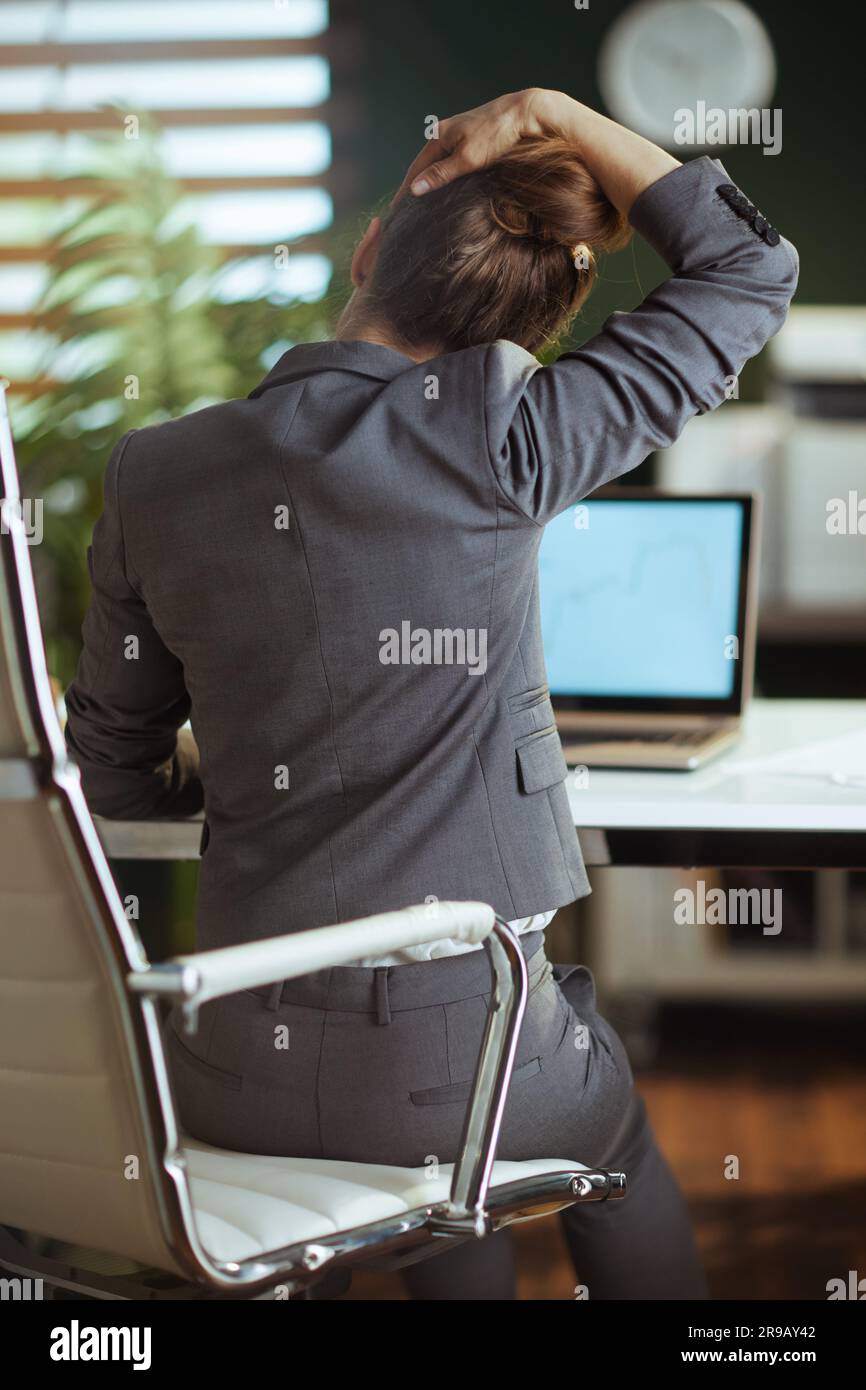 Ambiente di lavoro sostenibile. Vista da dietro la moderna donna proprietaria di una piccola impresa in abito da lavoro grigio in un moderno ufficio verde che si stende sul collo. Foto Stock