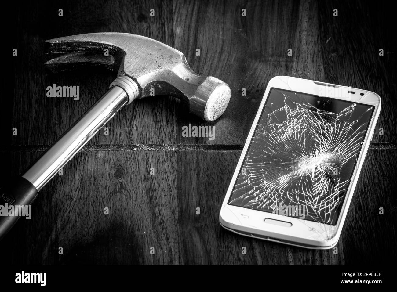 Smartphone rotto e un martello su un tavolo Foto Stock