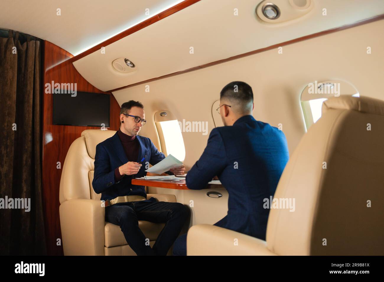 Due coppie di uomini d'affari sedute all'interno di un aereo privato a reazione e parlando di lavoro che stringono la mano, mentre si trova in volo il concetto di business della compagnia aerea Travel Foto Stock