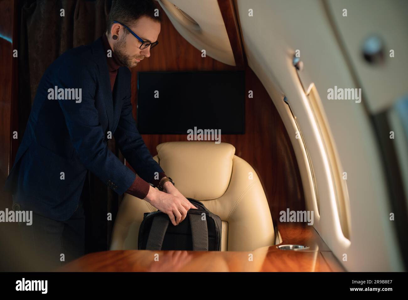 Primo piano elegante uomo d'affari tira fuori un computer portatile moderno e lo posiziona sul tavolo per lavorare da un aereo jet privato di prima classe Foto Stock