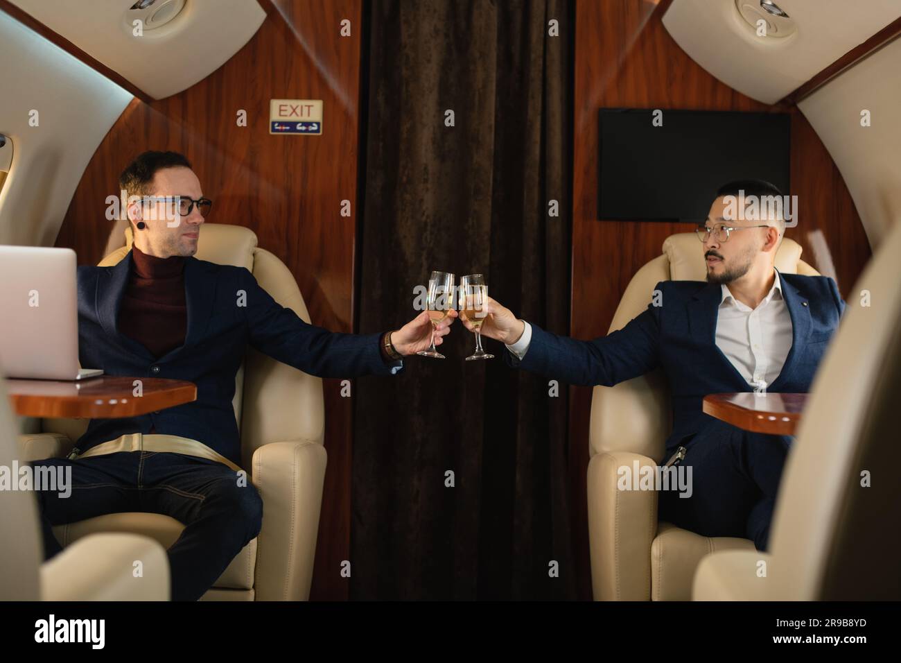 Due coppie di uomini d'affari di mezza età di successo sedute all'interno di un aereo privato e sorseggiate champagne durante il volo Foto Stock