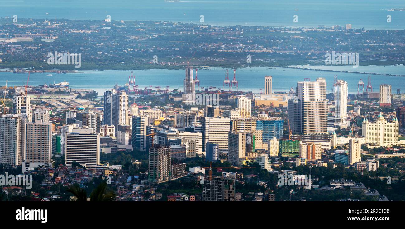 Prima del tramonto la luce del sole bagna gli edifici più alti della capitale di Cebu, guardando attraverso il canale del mare fino all'Isola di Maktan, sopra le palme e il lussureggiante fogliame Foto Stock