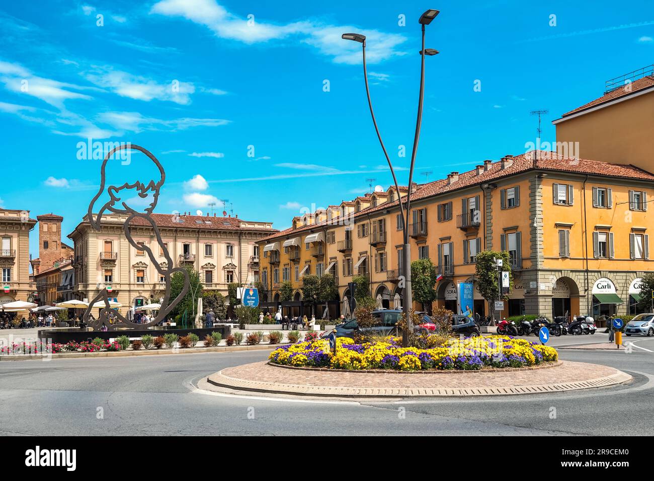 Lampione sulla rotonda decorato con fiori come piazza centrale con sculture moderne tra edifici storici sullo sfondo ad Alba, Italia. Foto Stock