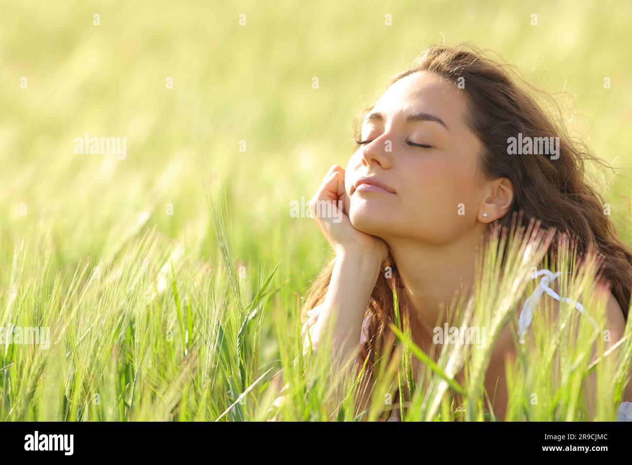 Donna che chiude gli occhi rilassa la mente in un campo verde al tramonto Foto Stock