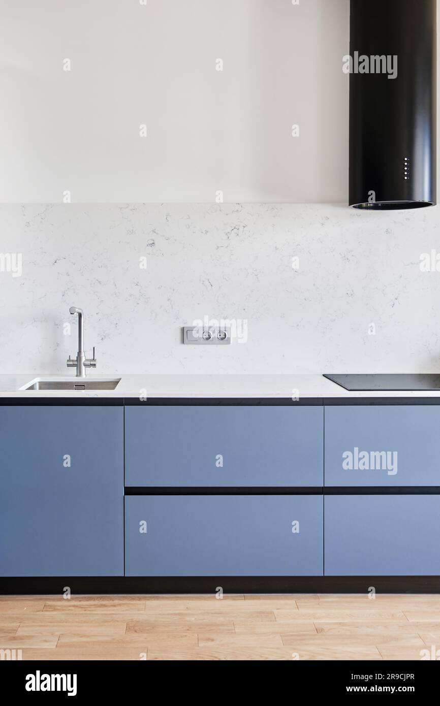 Una cucina moderna con scintillanti attrezzature per la casa, tra cui un aspiratore e un rubinetto per lavandino, presenta un pavimento elegante sotto i mobili. Foto Stock
