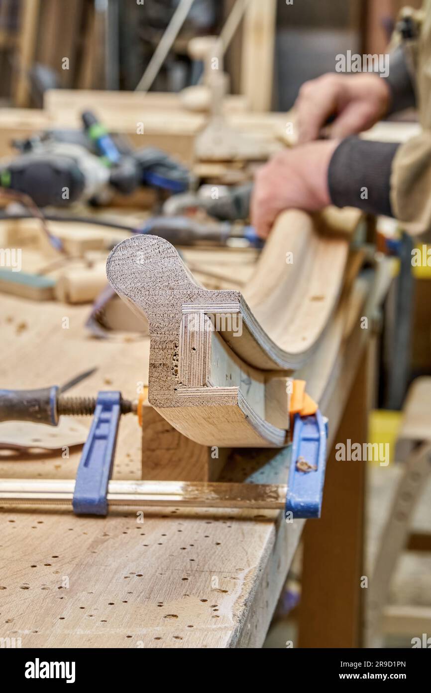 Carteggiatura per carpentiere che piega la ringhiera in legno con carta vetrata in primo piano. Senior master realizza dettagli con scala a chiocciola per gli interni della casa Foto Stock