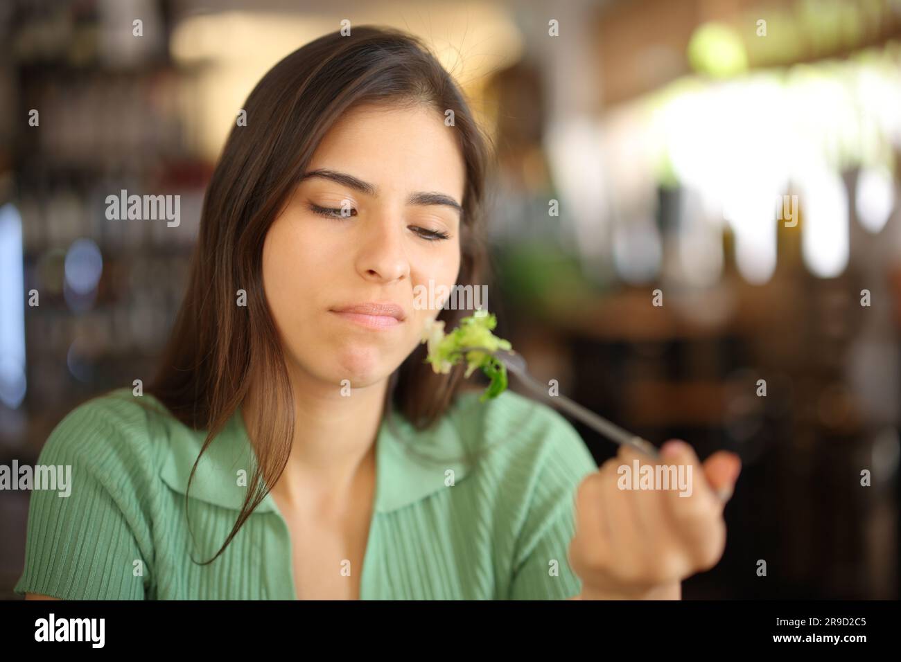 Donna disgustata che mangia lattuga seduta in un ristorante Foto Stock