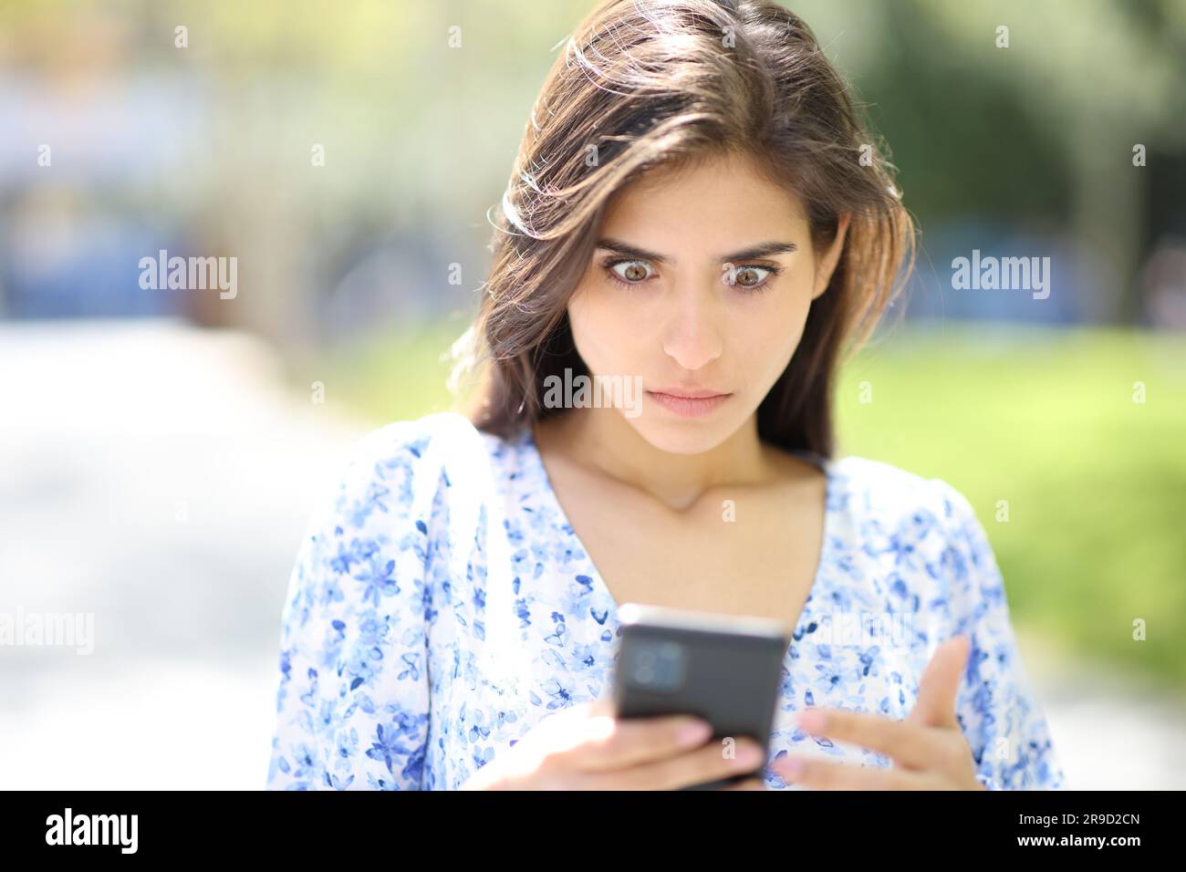Ritratto frontale di una donna perplessa che controlla il telefono notizie sorprendenti per strada Foto Stock