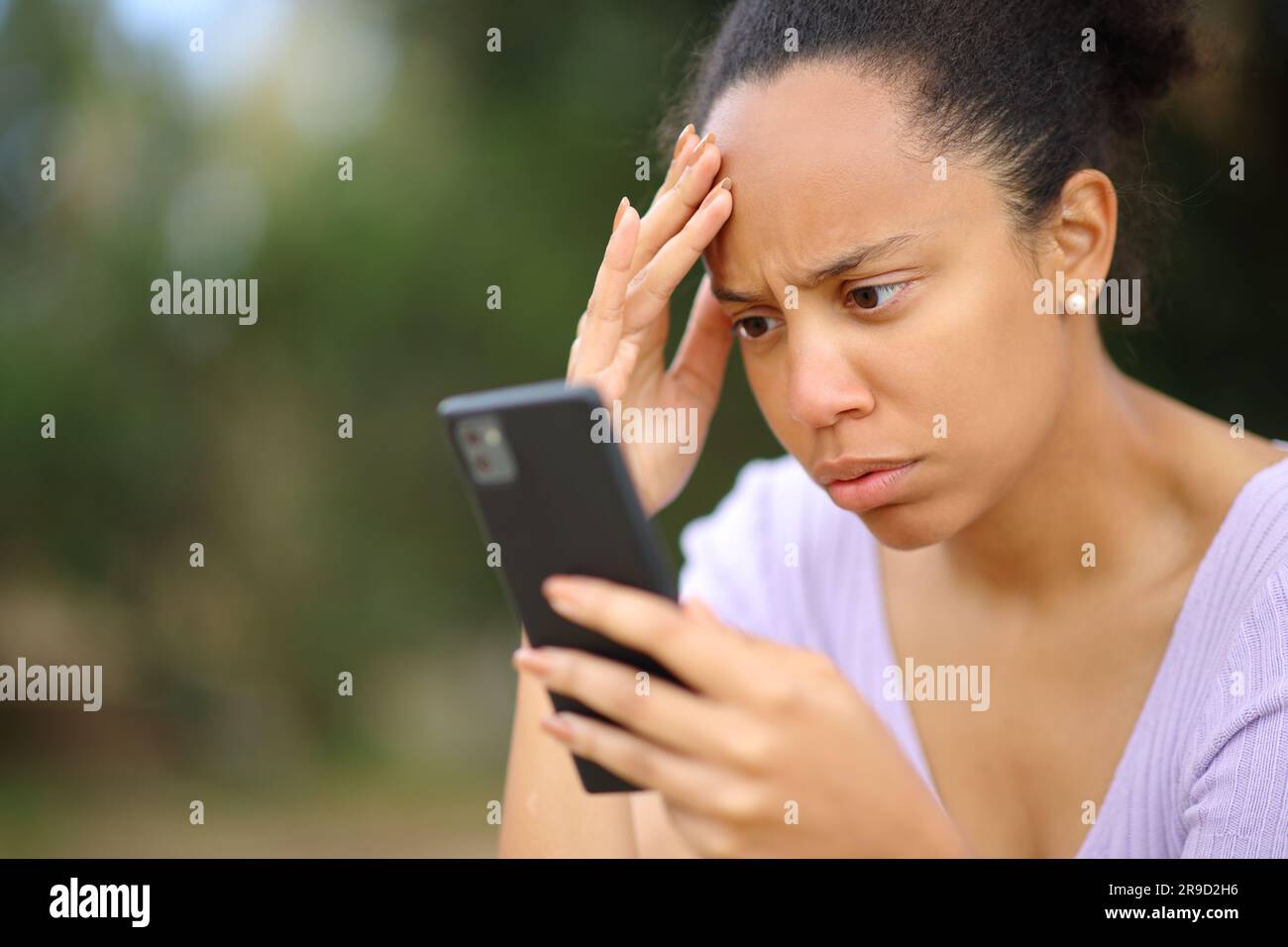 Preoccupata donna nera che controlla cattive notizie sul cellulare in un parco Foto Stock
