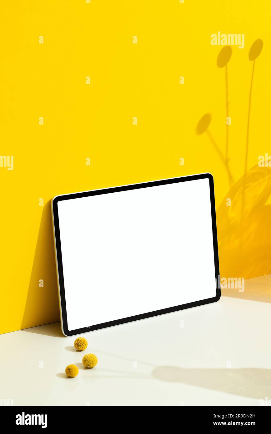 Mockup digitale per tablet con schermo bianco vuoto su sfondo giallo con ombre floreali Foto Stock