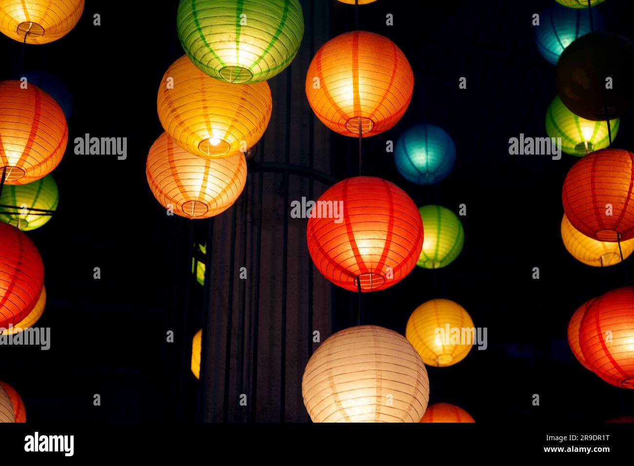 Molte lanterne di carta cinesi rotonde appese al buio. Molte decorazioni colorate e festose preparate per una celebrazione in stile orientale Foto Stock