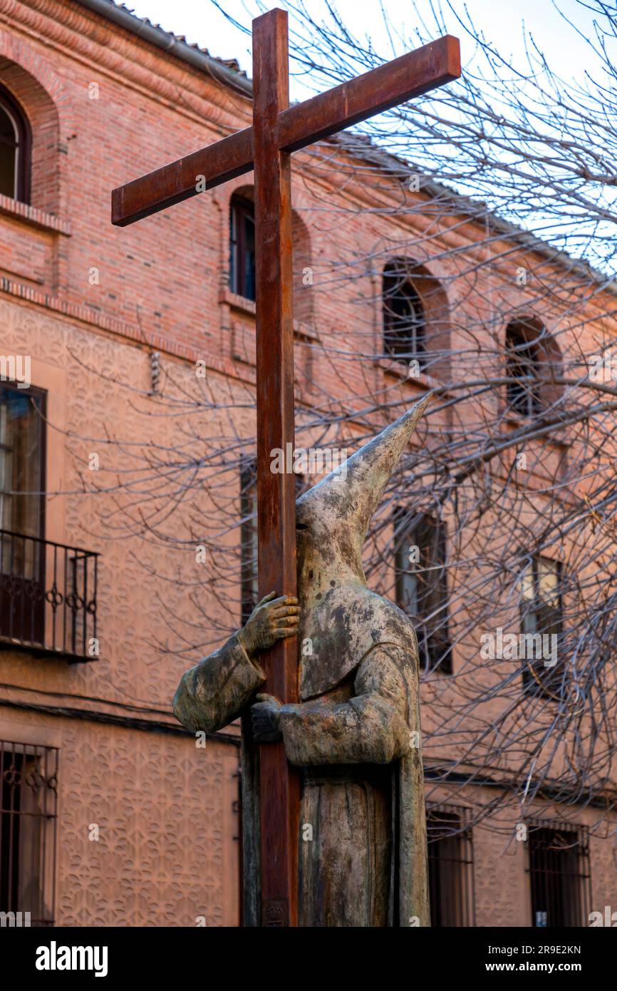 Segovia, Spagna - 18 febbraio 2022: Statua dell'uomo che tiene una grande croce, indossa un tradizionale abito cerimoniale con cappello a punta e maschera. Foto Stock