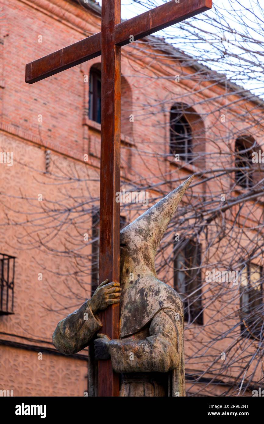 Segovia, Spagna - 18 febbraio 2022: Statua dell'uomo che tiene una grande croce, indossa un tradizionale abito cerimoniale con cappello a punta e maschera. Foto Stock