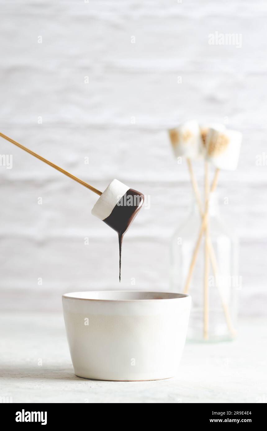 Un marshmallow bianco che gocce di cioccolato e alcuni marshmallow in bottiglia, su sfondo bianco. Foto Stock