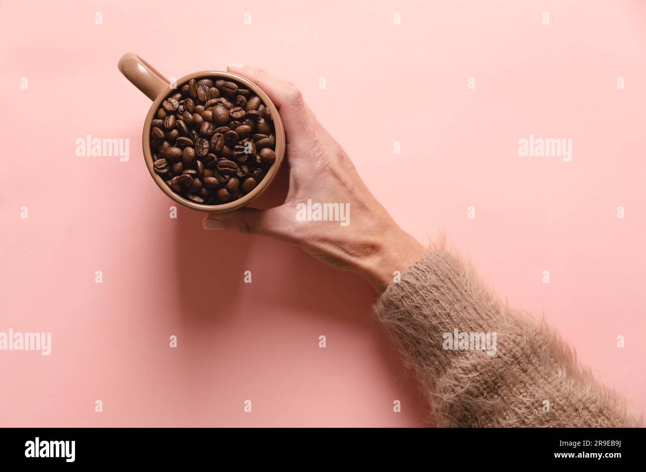 Mano femminile che tiene una tazza di chicchi di caffè su sfondo rosa. Vista dall'alto. Foto Stock