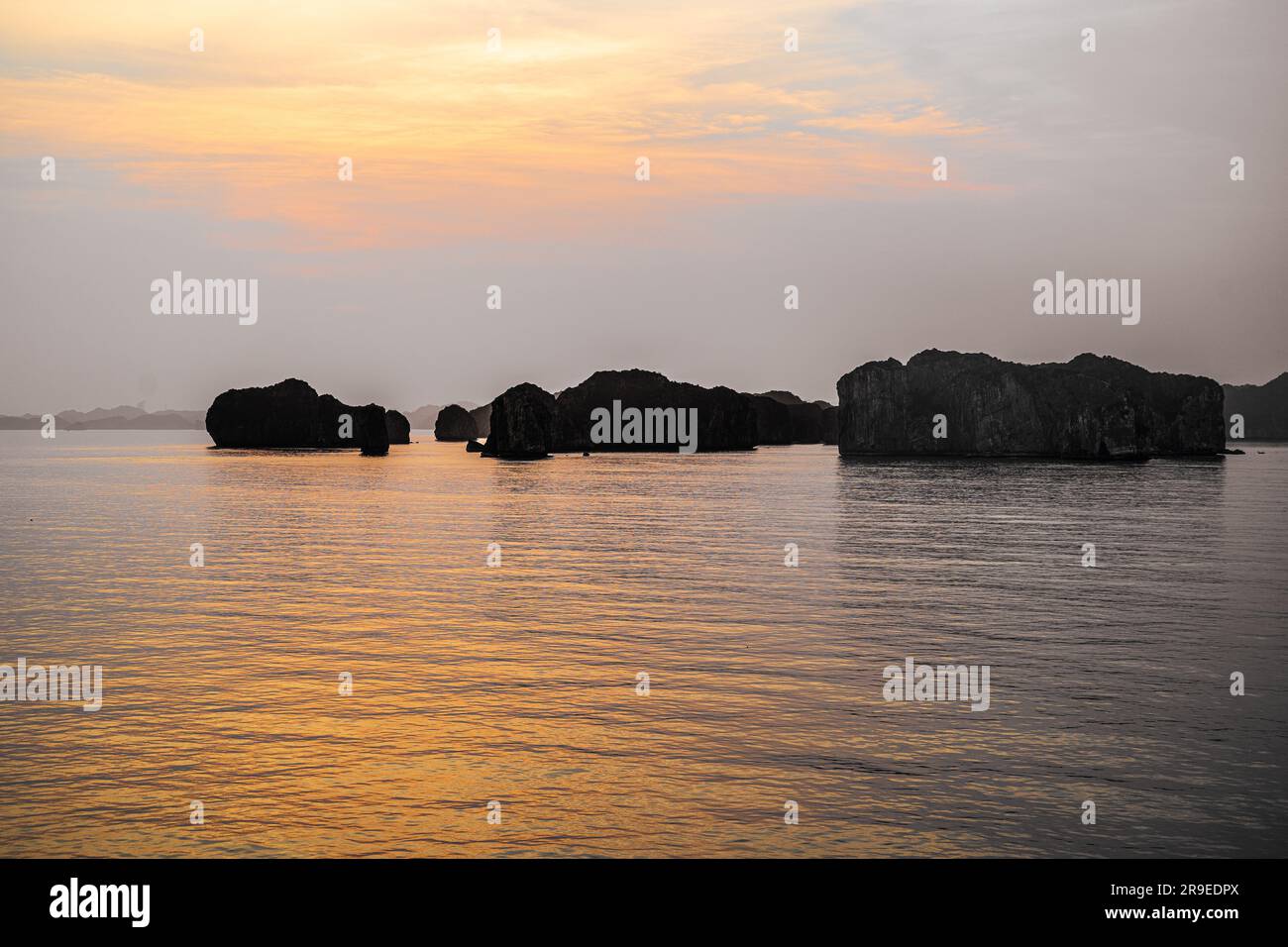 Foto che si affaccia sulla baia di ha Long mentre il sole tramonta e le formazioni rocciose retroilluminate diventano sagome Foto Stock