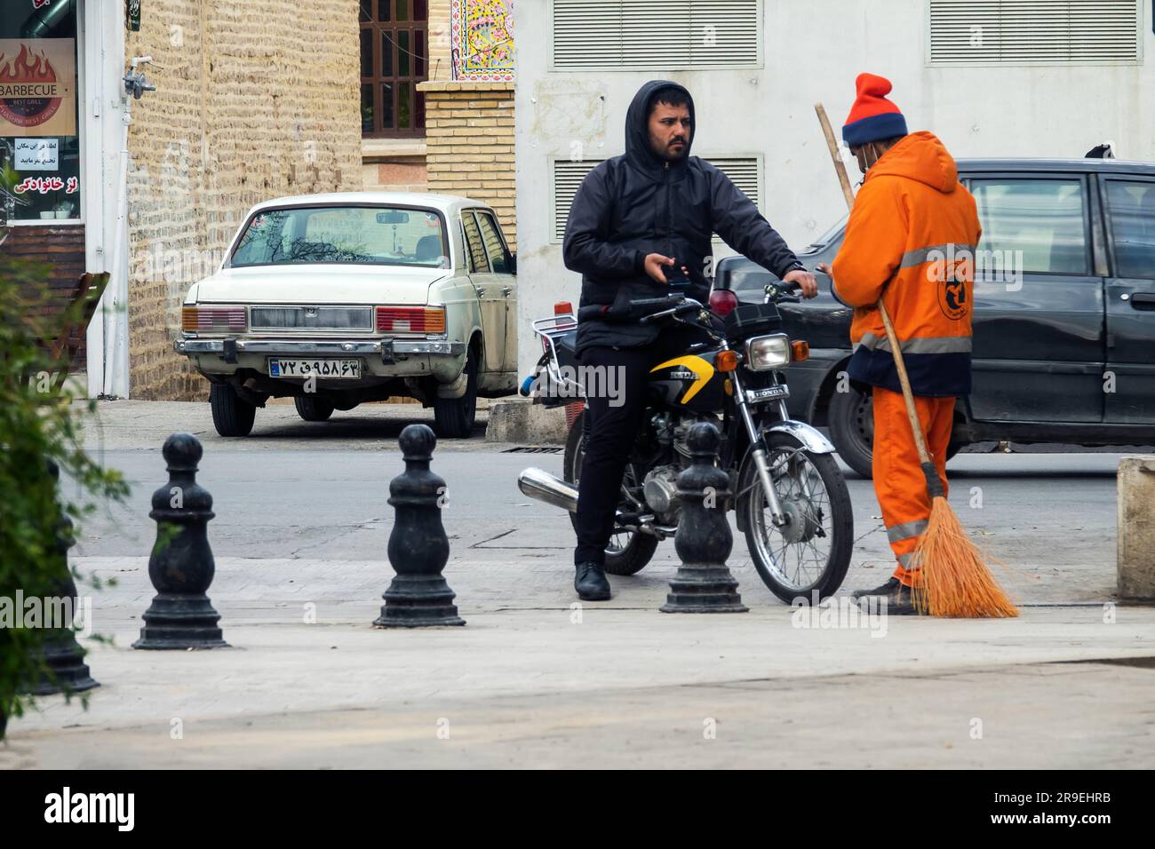 Shiraz, Iran - 31 dicembre 2022: Vita quotidiana degli iraniani. Un motociclista iraniano su una moto cinese parla con un cameriere in tuta Foto Stock