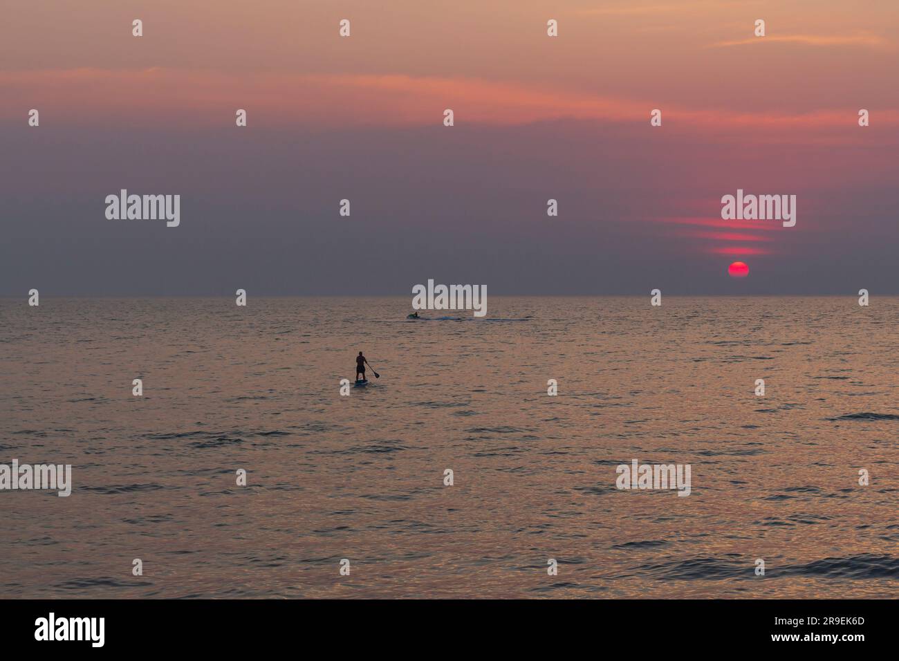 Solitario uomo di bordo SUP, Surfer naviga sull'acqua di mare verso il tramonto, avventure in mare. sagoma di turista maschile su paddle board sotto trop Foto Stock