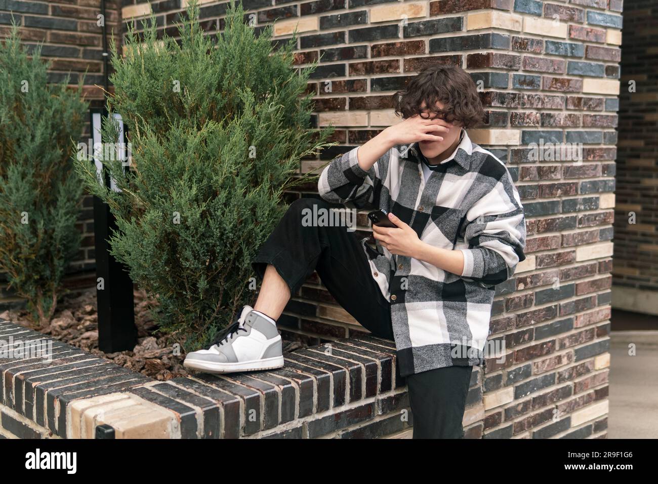 giovane uomo in città seduto sul marciapiede con un telefono che fa una palma Foto Stock