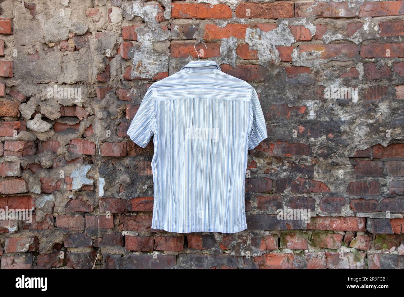 camicia estiva a righe leggere uomo appesa a una parete in mattoni all'aperto, abbigliamento uomo Foto Stock