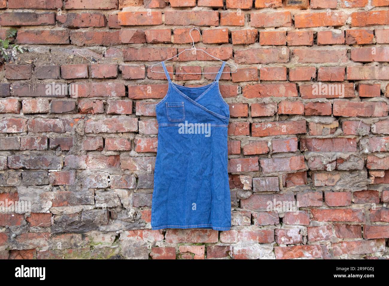 abito da donna blu denim appeso a un appendiabiti su un muro di mattoni in strada, abbigliamento da donna alla moda Foto Stock