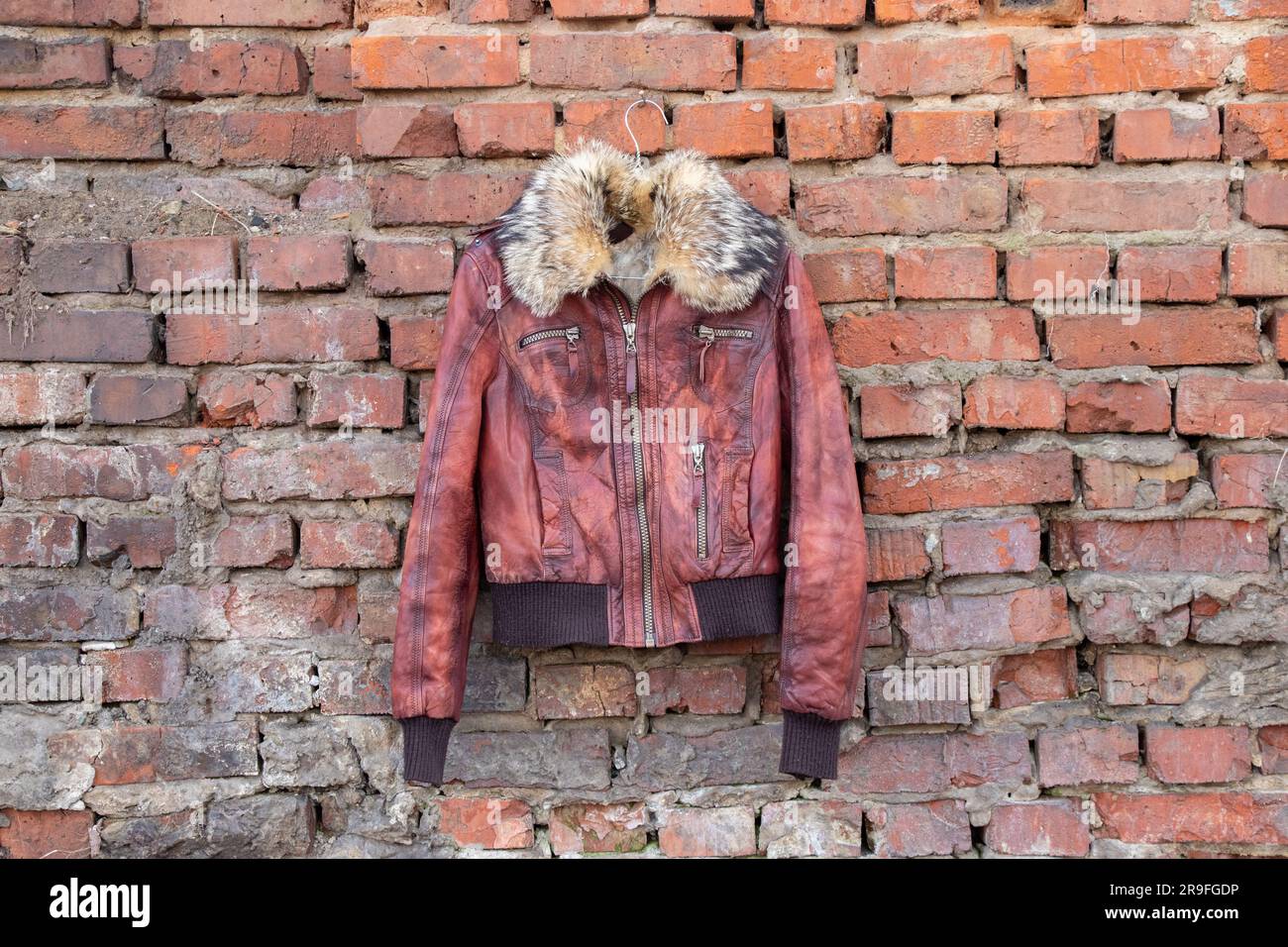 giacca invernale donna in pelle di pelliccia rossa appesa su un appendiabiti su una vecchia parete di mattoni all'aperto durante il giorno, abbigliamento femminile Foto Stock
