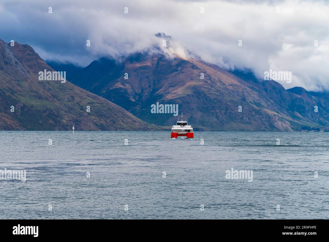 Fotografia di un traghetto d'acqua rossa e bianca sul lago Wakatipu a Queenstown con montagne sullo sfondo sull'Isola del Sud della nuova Zelanda Foto Stock