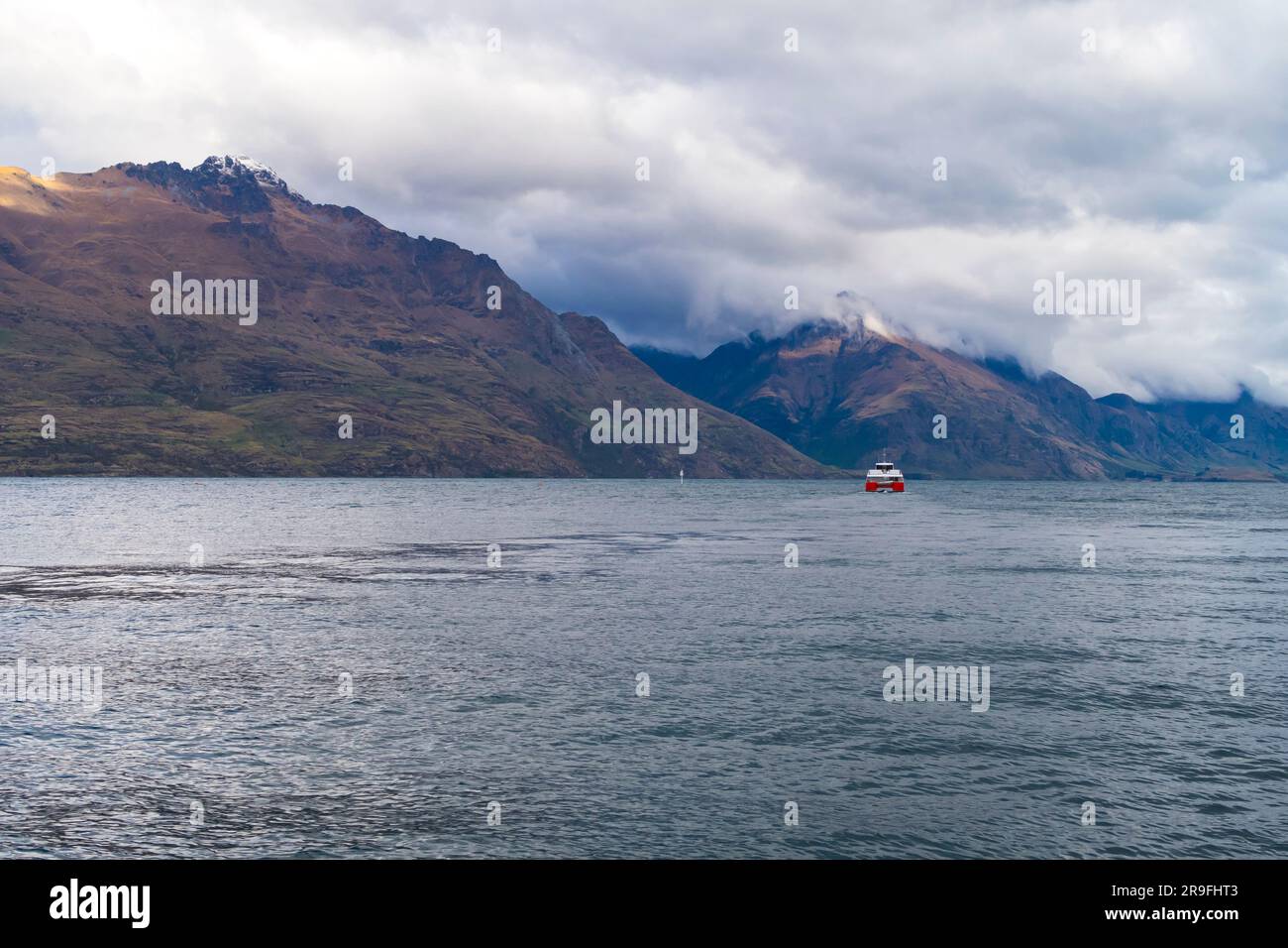 Fotografia di un traghetto d'acqua rossa e bianca sul lago Wakatipu a Queenstown con montagne sullo sfondo sull'Isola del Sud della nuova Zelanda Foto Stock