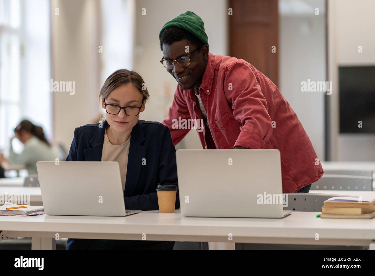 Un ragazzo afroamericano aiuta le studentesse caucasiche a lavorare su un progetto nell'università universitaria. Foto Stock