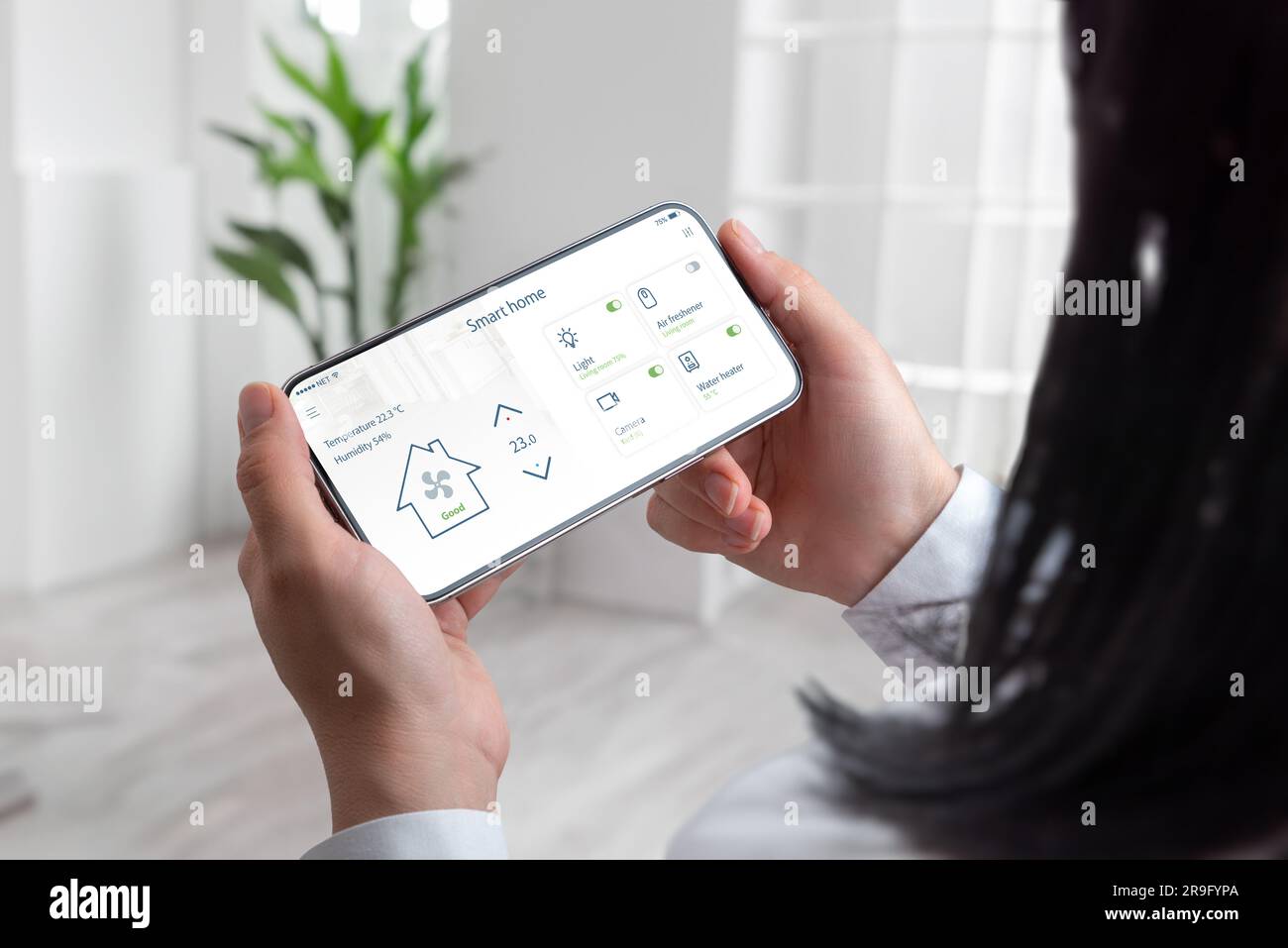 La vita moderna come donna gestisce senza fatica la sua casa intelligente utilizzando un telefono cellulare e lo sfondo del soggiorno Foto Stock