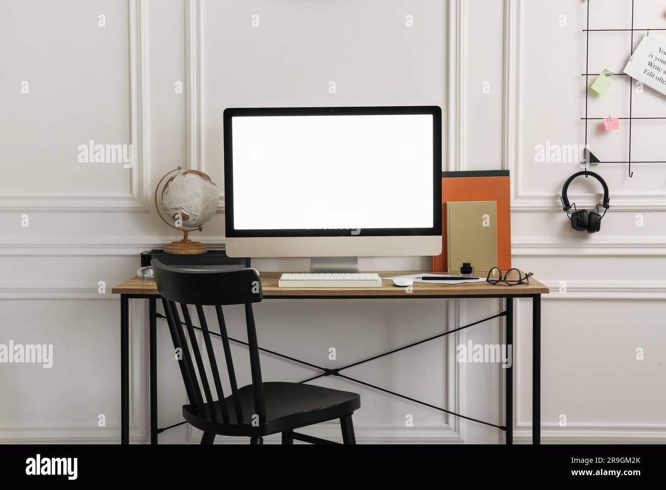 Elegante area di lavoro con computer e cancelleria su una scrivania in legno vicino a pareti bianche all'interno Foto Stock