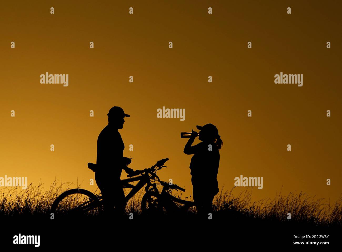 Cyclists take a water break during an evening ride, Monday, June 26, 2023, in San Antonio. Meteorologists say scorching temperatures brought on by a heat dome have taxed the Texas power grid and threaten to bring record highs to the state. (AP Photo/Eric Gay) Foto Stock