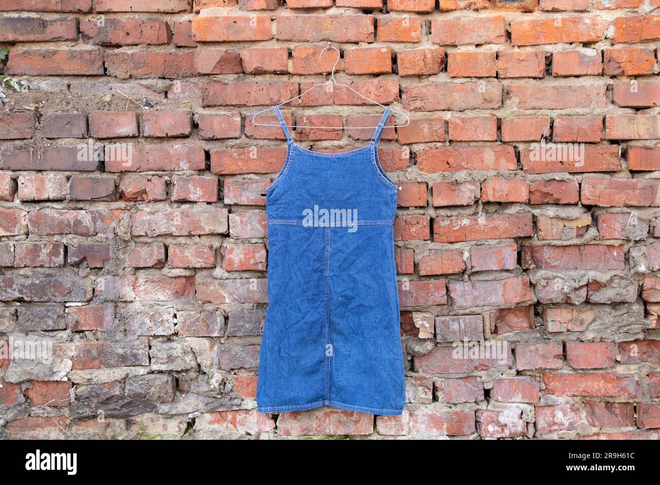 abito da donna blu denim appeso a un appendiabiti su un muro di mattoni in strada, abbigliamento da donna alla moda Foto Stock
