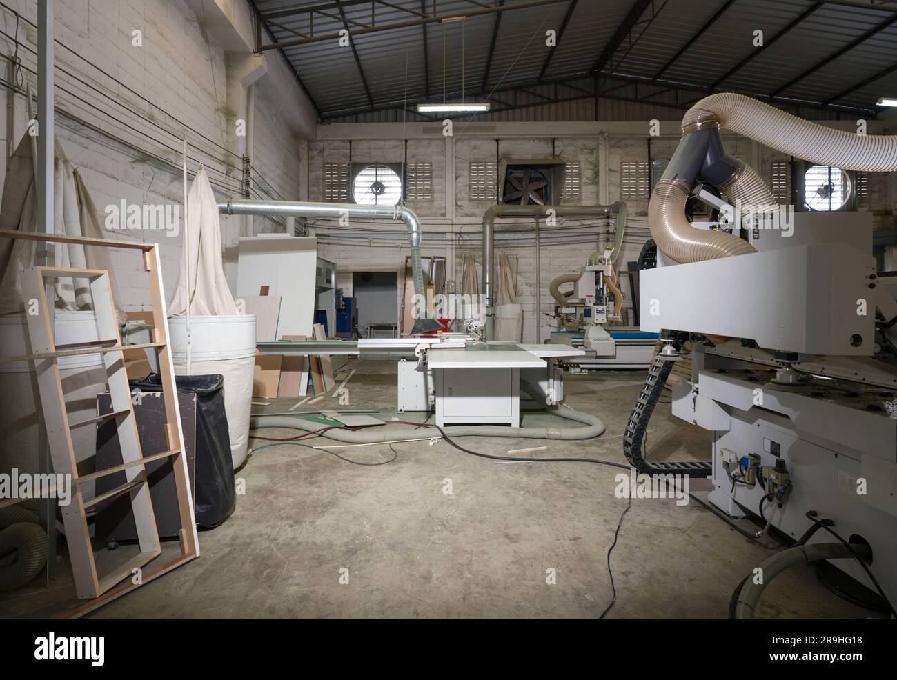 Atmosfera all'interno di una fabbrica di mobili in legno con pile di compensato e macchinari moderni. Le ventole di scarico si trovano su una parete leggera in mattoni di calcestruzzo nella b Foto Stock