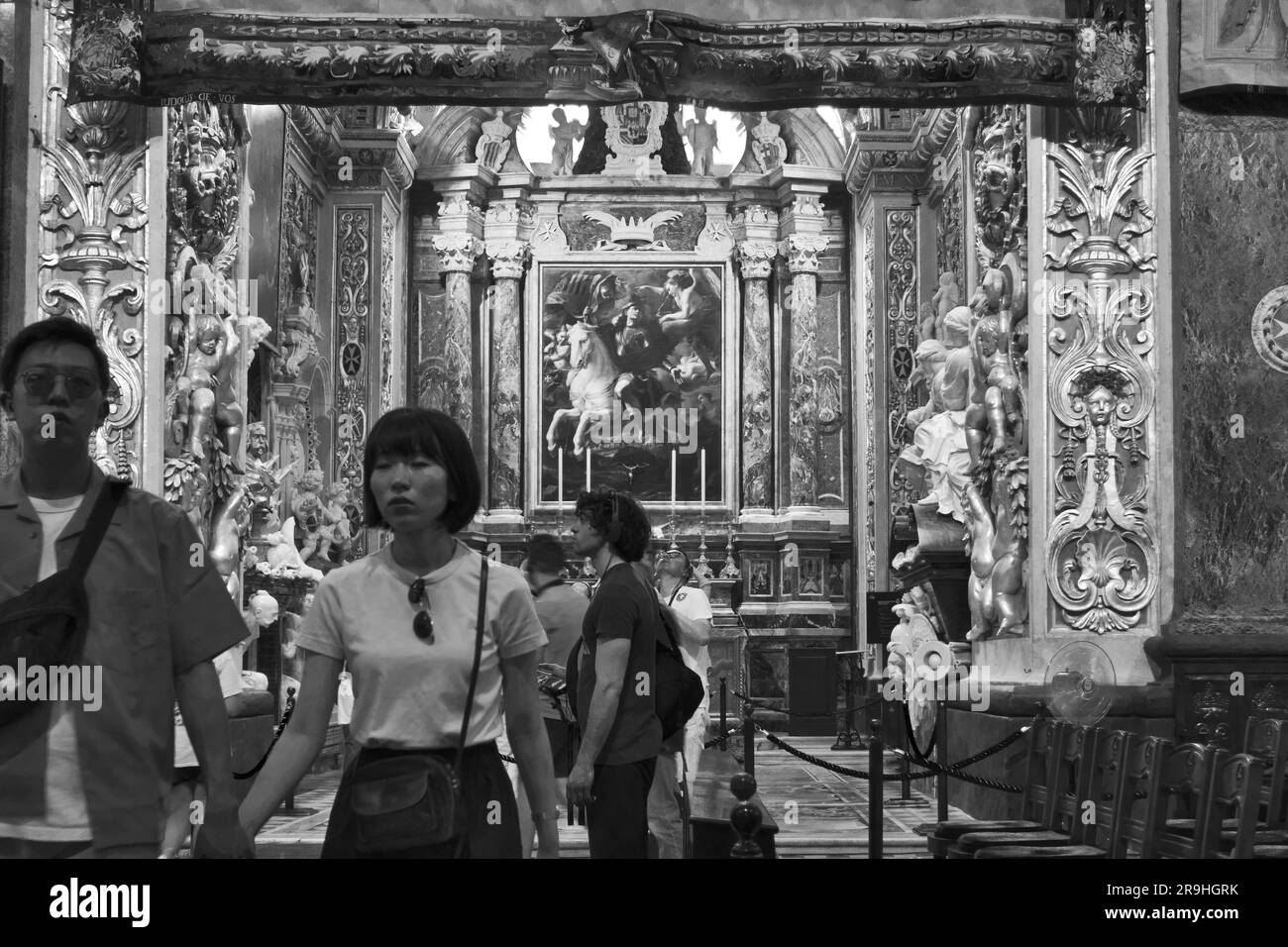 Una coppia di turisti asiatici sfocati in bianco e nero esce dalla Chapel of the Langue of Aragon all'interno di St Co-cattedrale di Giovanni a la Valletta, Malta Foto Stock